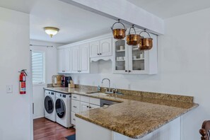 A kitchen with white cabinets, a granite countertop, a washing machine, and copper hanging pots. - Steps to Ski Trail, Fireplace - Kingswood 1B (Quechee)