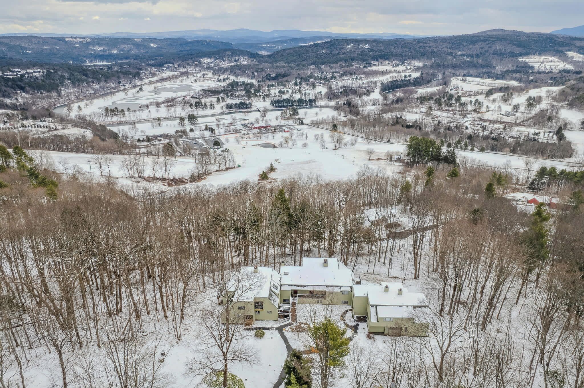 A snow-covered landscape with a large building complex featuring multiple structures, surrounded by trees and open fields.
