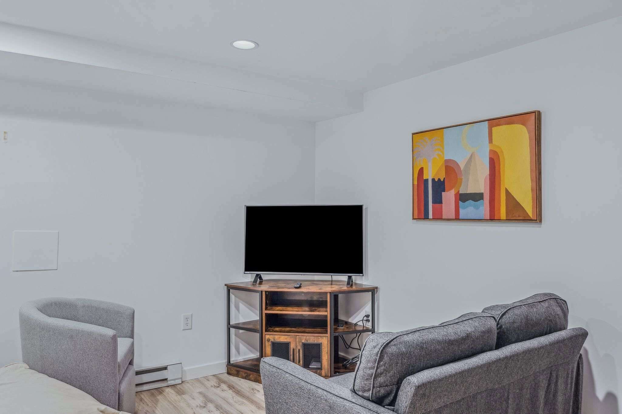 Una sala de estar moderna con un televisor de pantalla plana sobre un soporte de madera, sofás grises y un cuadro abstracto y colorido en la pared.