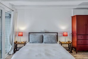 Une chambre à coucher avec un lit, deux tables de chevet avec des lampes, une armoire rouge et une porte-fenêtre coulissante.