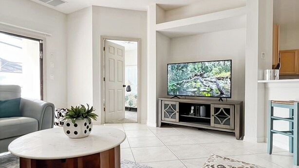 A modern living room with a round coffee table, a leopard print ottoman, a television on a cabinet, and a door leading to another room.