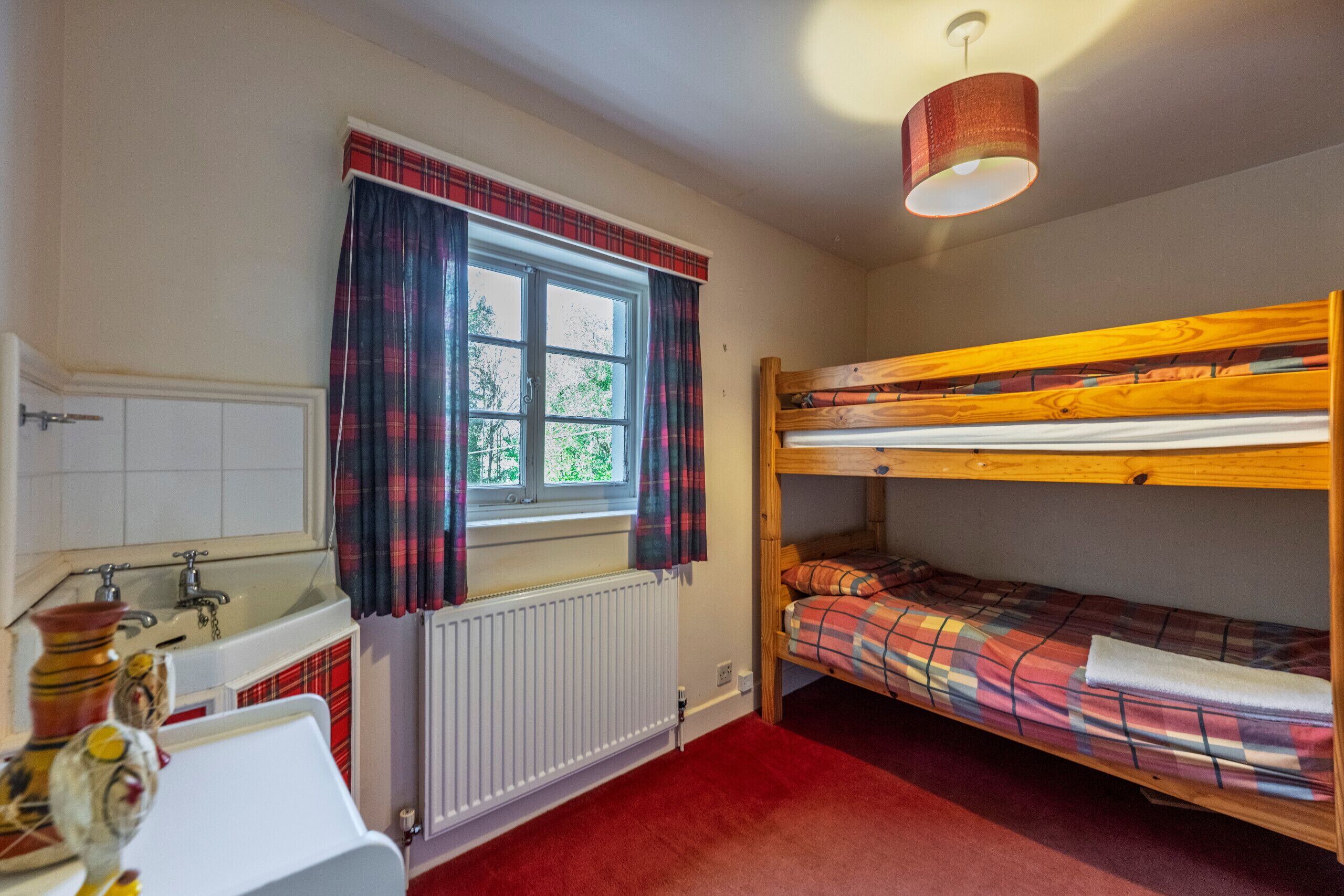 A room with a window, a radiator, a sink, and a bunk bed.