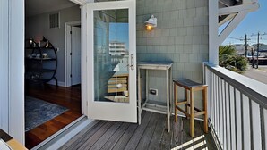 An open door leading to a balcony with a wooden floor, a small table, and a chair.