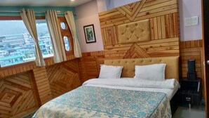 Ein Schlafzimmer mit Holz-Kopfteil, einem Bett mit weißer Bettwäsche, einem Fenster mit Vorhängen und Blick auf die Stadt.