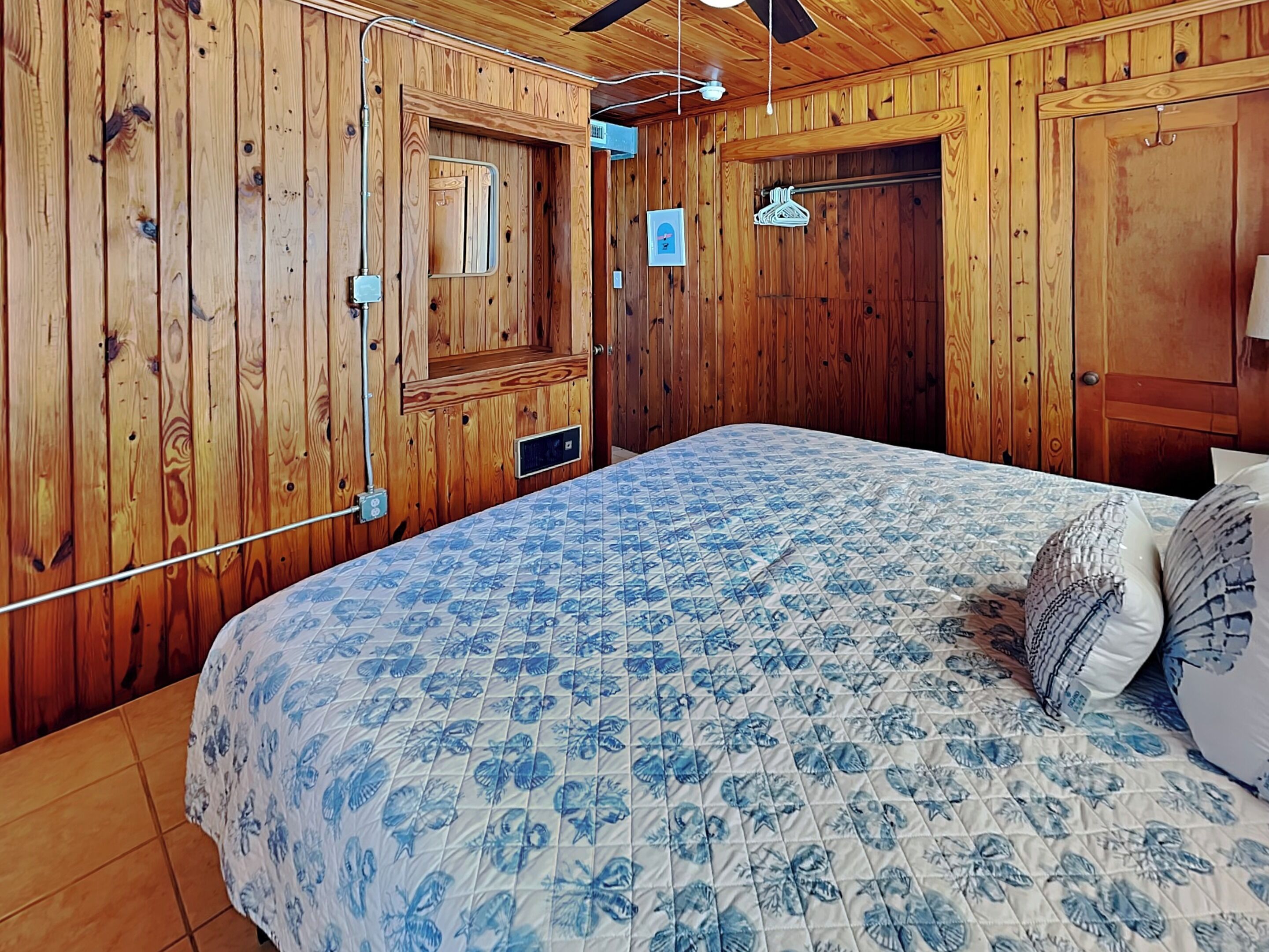 Een slaapkamer met houten lambrisering, een bed, een plafondventilator en een deur met een raam.