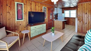 A wooden interior with a sofa, TV, small table, and kitchenette. - Sea Glass Suites #3 | Beach Nearby, Pet-Friendly (Topsail Beach)