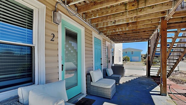 A covered porch with wicker furniture and a blue door. - Sea Glass Suites #3 | Beach Nearby, Pet-Friendly (Topsail Beach)
