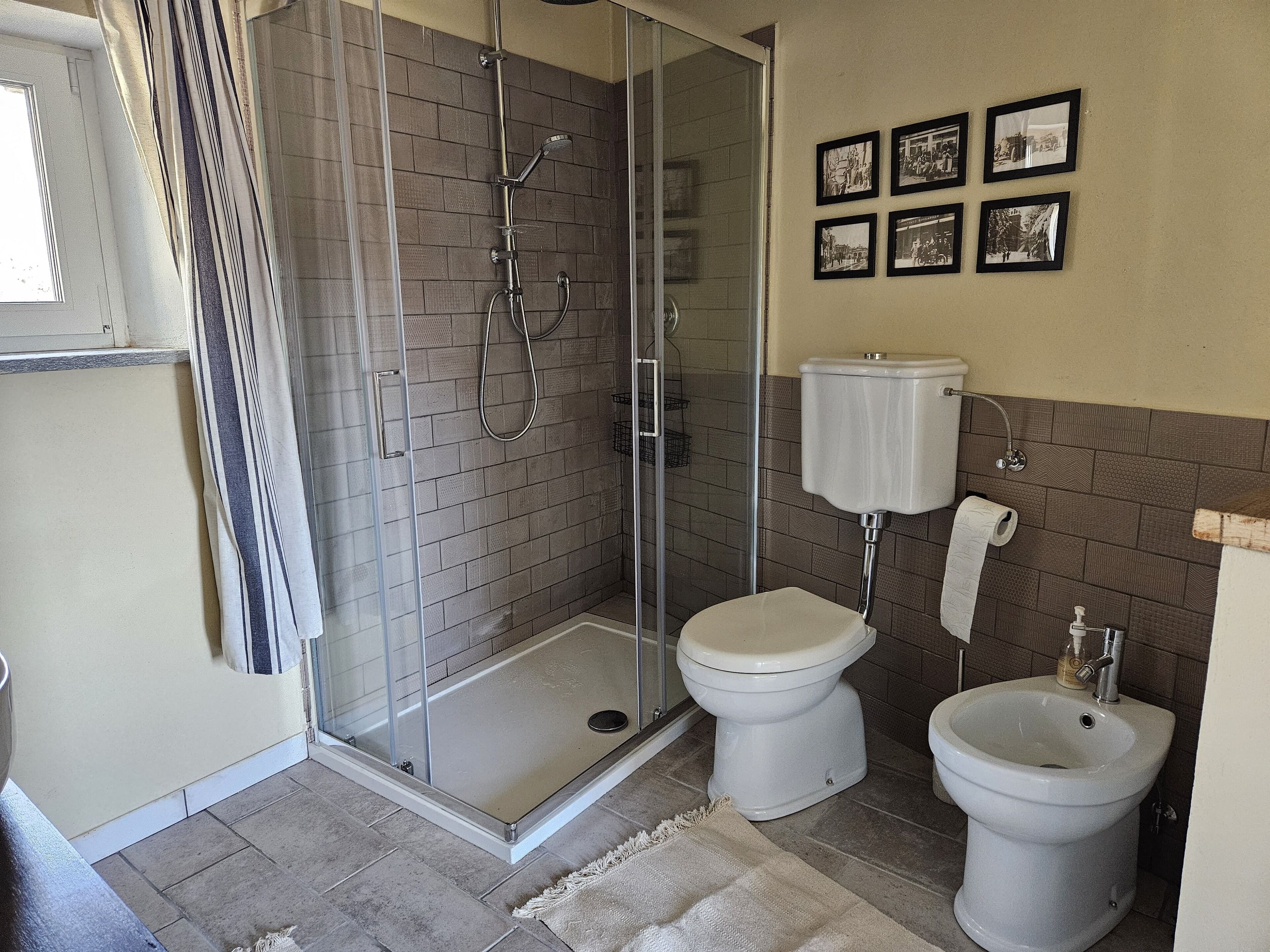 A bathroom with a glass-enclosed shower, a toilet, and a bidet. There are framed pictures on the wall.