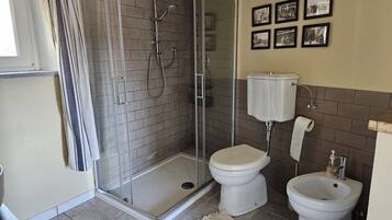 A bathroom with a glass-enclosed shower, a toilet, and a bidet. There are framed pictures on the wall.