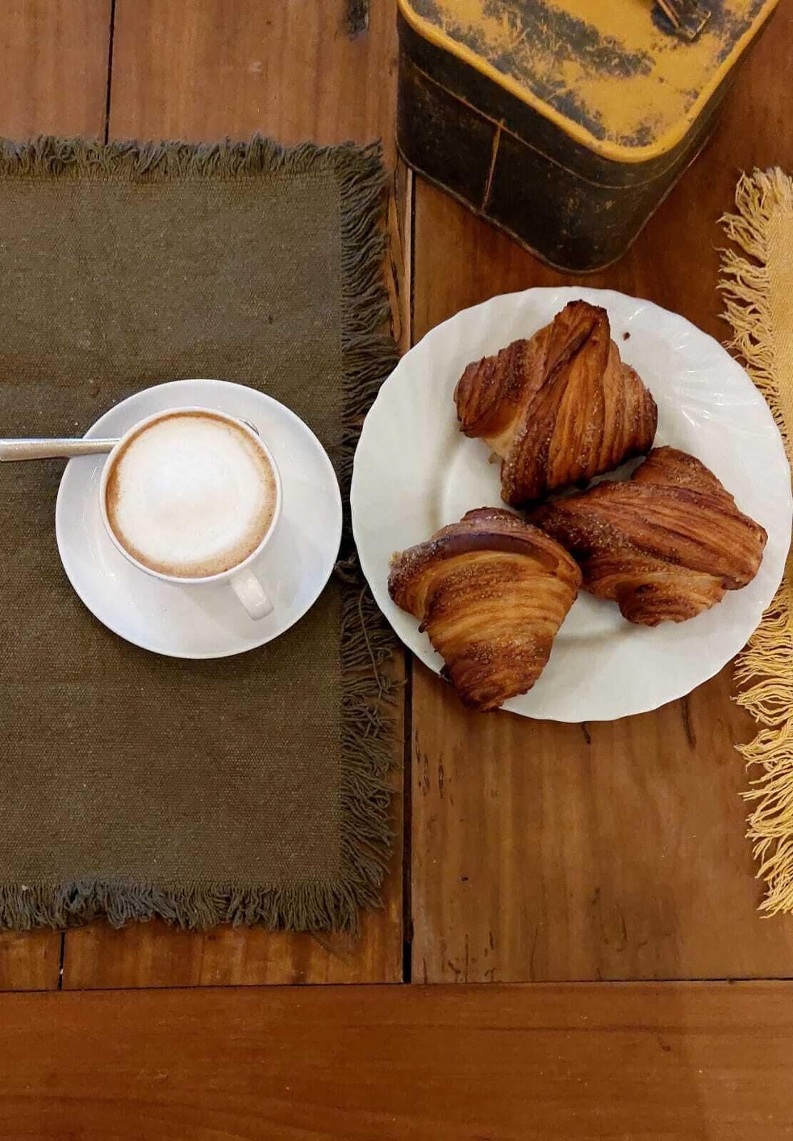Una mesa con una fuente de croissants y una taza de café sobre un mantel tejido.
