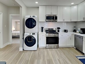 A modern kitchen with white cabinetry, a stainless steel stove, a microwave, and a washer-dryer unit.