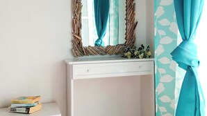 Een kamer met een wit bureau, een spiegel met een houten lijst en een blauwgroen gordijn.