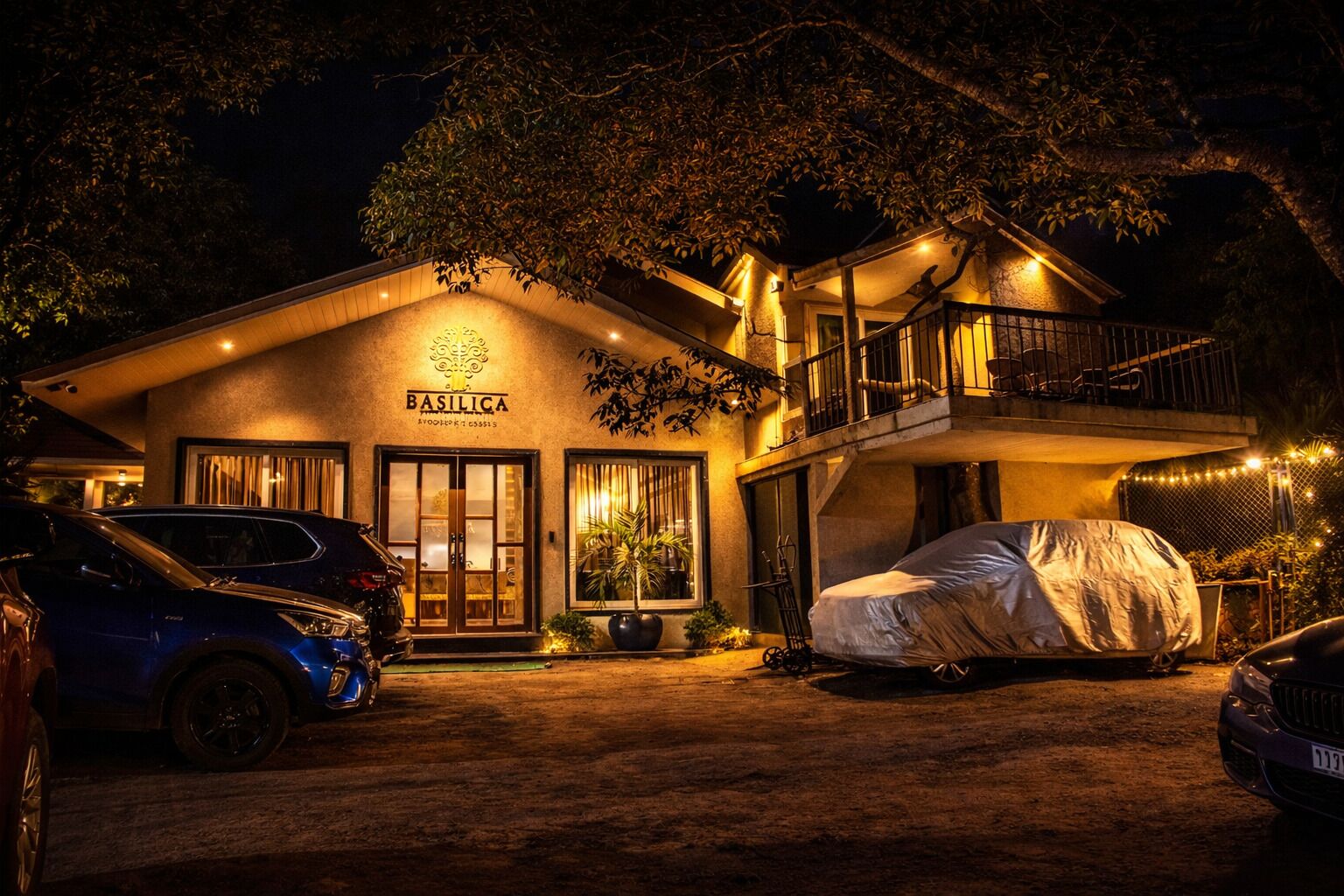 A hotel named 'BASILICA' with a covered carport, a balcony, and a well-lit entrance.