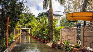 A wet pathway lined with potted plants and a building in the background. - Basilica Resort - Where Luxury Redefines (Panchgani)