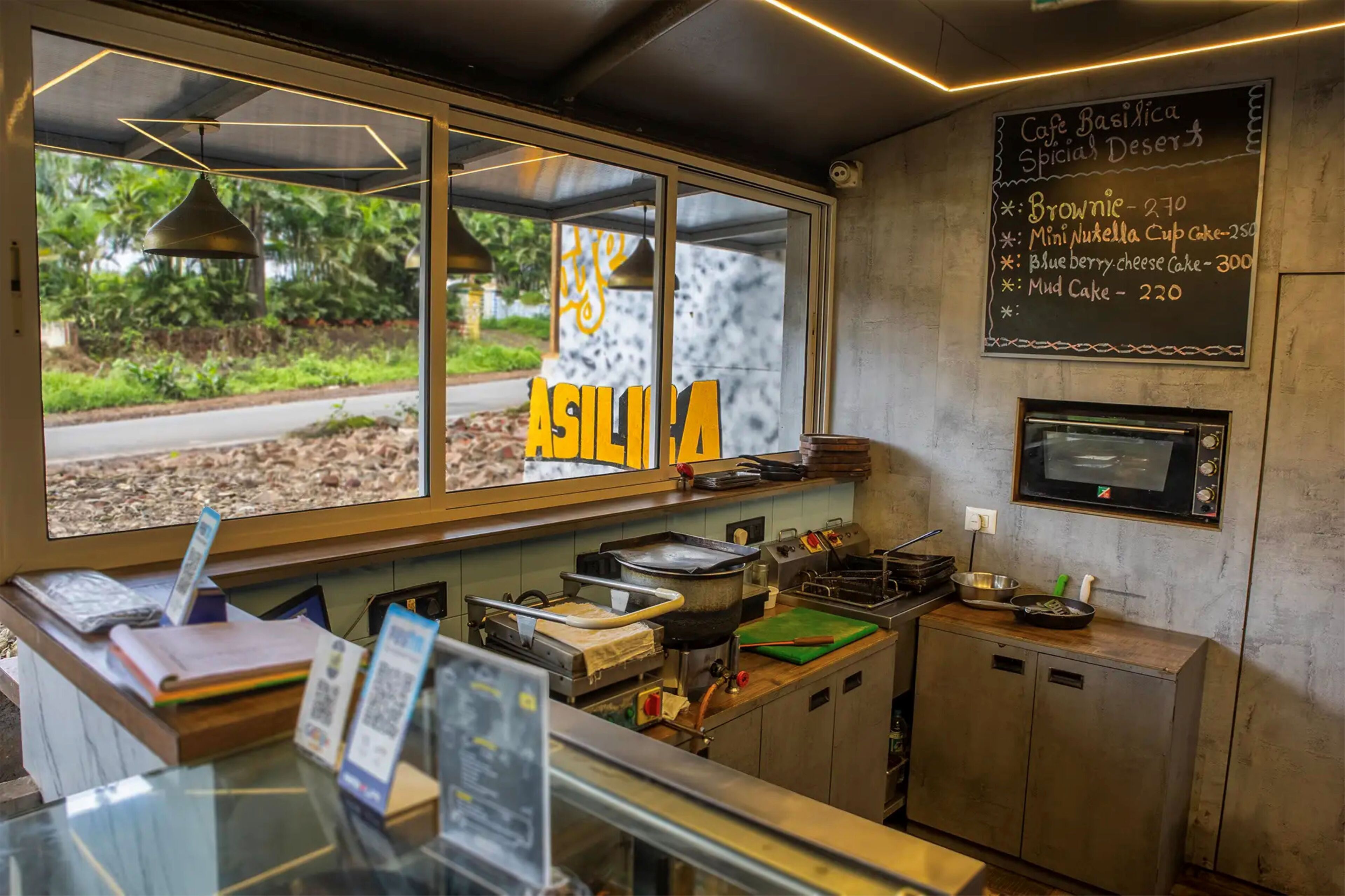A cafe with a menu board listing desserts, a window with the word "ASILHA" visible, and kitchen equipment.