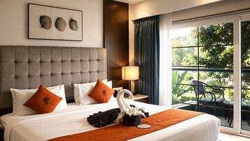 Habitación de hotel con una cama grande, cabecero, mesita de noche con lámpara y vista a zonas verdes por la ventana.