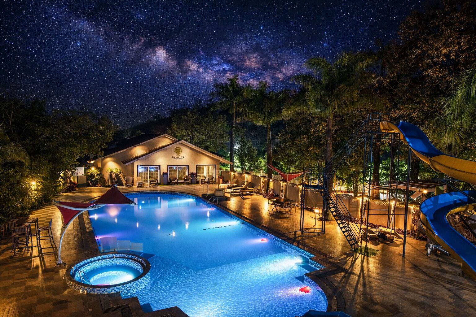 Una piscina con tobogán, un edificio con letrero y un cielo nocturno estrellado.