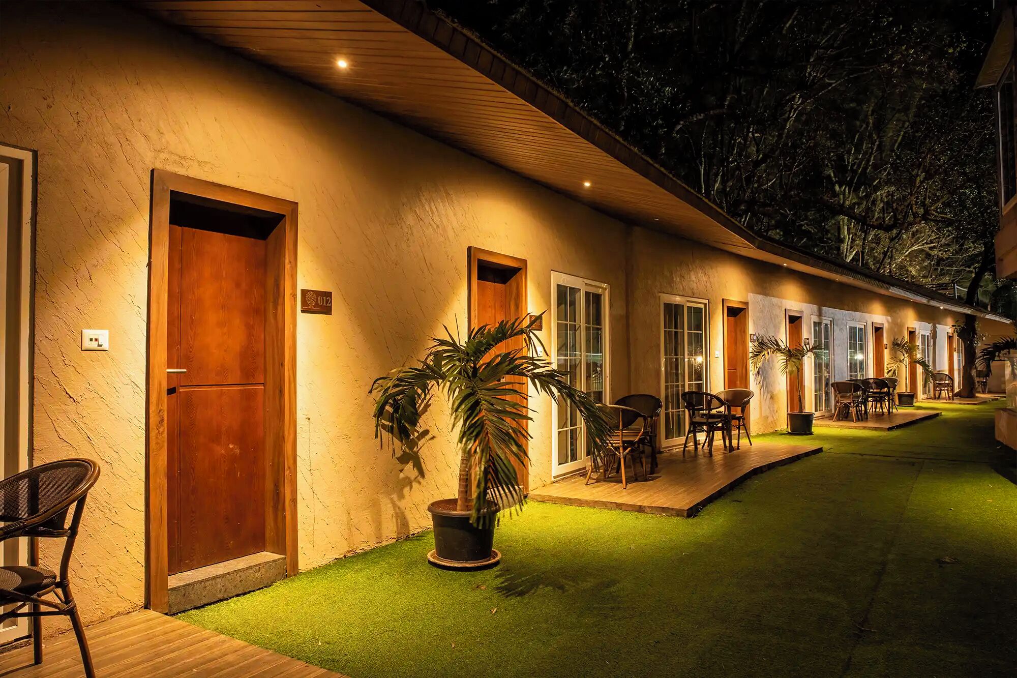 A hotel corridor with wooden doors, potted plants, and outdoor seating.