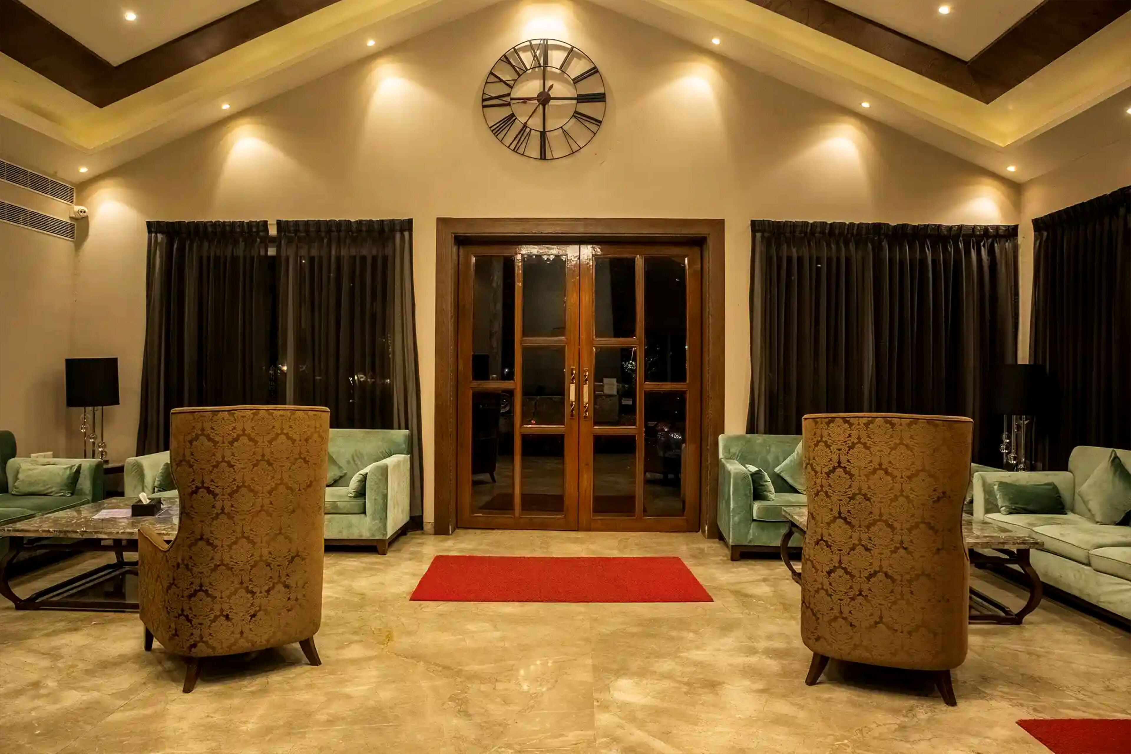 A spacious living area with two patterned armchairs, a large clock, and a glass door entrance.