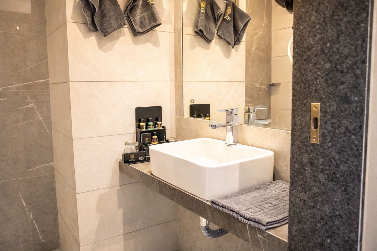 A modern bathroom with a large mirror, a white sink, and a towel rack.