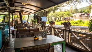 An outdoor restaurant with tables and chairs, a covered area, and a view of greenery and buildings in the background. - Basilica Resort - Where Luxury Redefines (Panchgani)