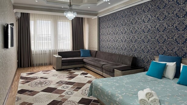 Una habitación de hotel moderna con sofá modular, cama con ropa de cama azul, alfombra estampada y decoración en la pared.