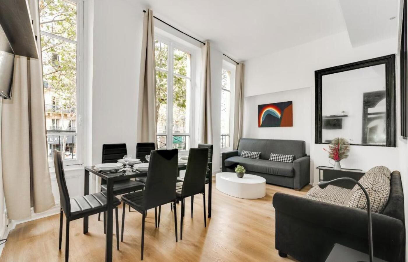 A modern living room with a dining area, large windows, a grey sofa, and a coffee table.
