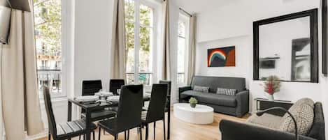 A modern living room with a dining area, large windows, a grey sofa, and a coffee table.