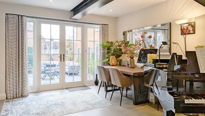 A dining area with a piano, a table with chairs, a vase with flowers, and a view through a glass door to an outdoor patio.
