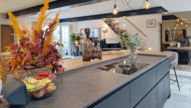 A modern kitchen with a central island, a dining area with a piano, and a staircase leading to another level.