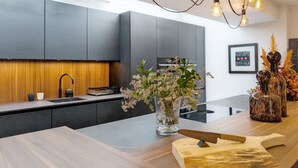A modern kitchen with grey cabinets, a wooden countertop, a central island with a knife, and a hanging light fixture.