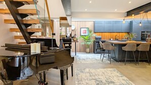 A modern living space with a grand piano, a staircase, a kitchen area, and a dining area.