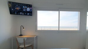 A bedroom with a bed, a desk with a chair, a TV mounted on the wall, and a large window with a beach view. - 🌊 Fenêtres sur Mer - Sea View & Garage - 3 bedrooms (Berck)