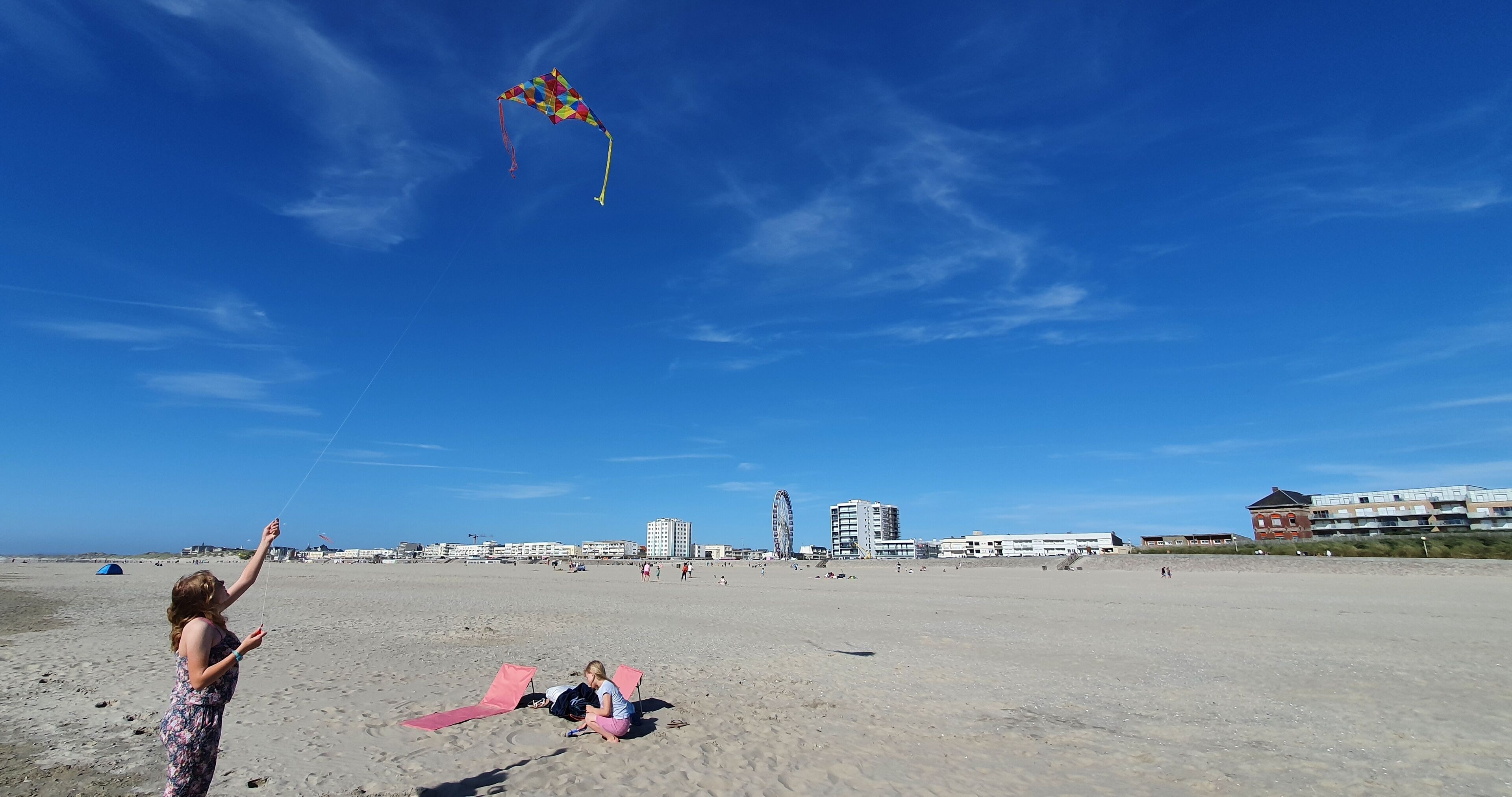 Una spiaggia con cielo sereno, un aquilone colorato e edifici sullo sfondo.