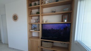 A wooden entertainment unit with a flat-screen TV, books, and decorative items. - 🌊 Fenêtres sur Mer - Sea View & Garage - 3 bedrooms (Berck)