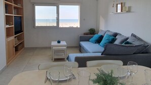 A living room with a sofa, dining table, and a window with a beach view. - 🌊 Fenêtres sur Mer - Sea View & Garage - 3 bedrooms (Berck)