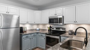 Una cocina moderna con armarios blancos, electrodomésticos de acero inoxidable, encimeras de granito y horno empotrado.