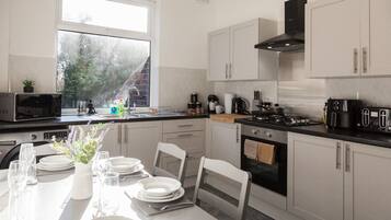 A modern kitchen with white cabinets, a black stove, and a dining area set for four.