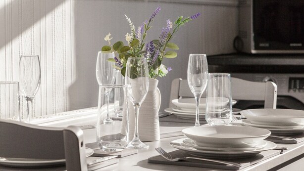 A dining table set with white plates, glasses, and cutlery, accompanied by a vase with flowers.