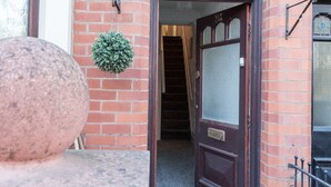 A red brick building with a dark wooden door and a small green plant hanging on the wall.
