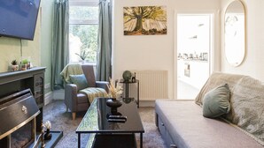 A living room with a TV, a fireplace, a sofa, a coffee table, and a window with curtains.