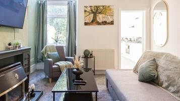 A living room with a TV, a fireplace, a sofa, a coffee table, and a window with curtains.