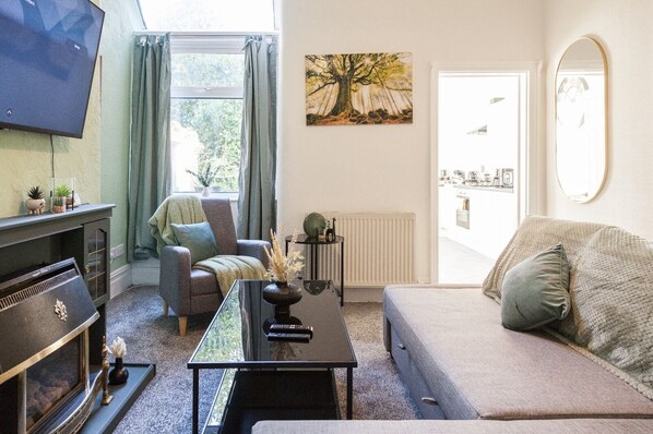 Una sala de estar con televisor, chimenea, sofá, mesa de centro y ventana con cortinas.