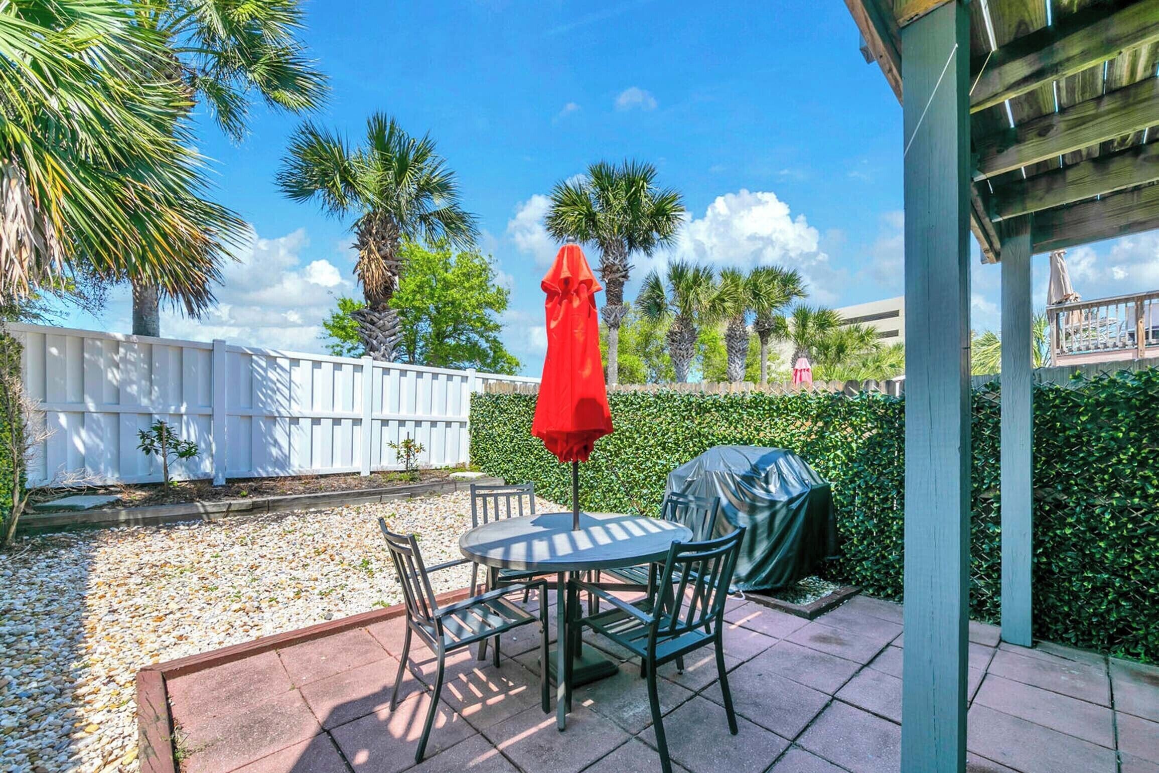 Une terrasse avec une table et des chaises, un parasol rouge et un espace barbecue abrité.