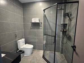 A modern bathroom with a glass-enclosed shower, a toilet, and a small shelf with toiletries.