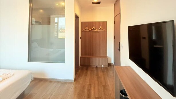 A modern hotel room with a large bed, a TV, a wooden bench, and a walk-in closet. - Xianglong Hotel (Luang Prabang)