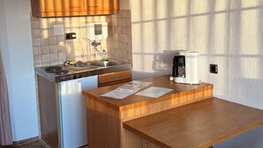 A compact kitchen with wooden cabinets, a built-in dishwasher, a coffee maker, and a sink. - In & Out boarding house comfort room (Stolberg)