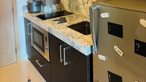 Una cocina moderna con armarios oscuros, encimera de mármol, horno empotrado y refrigerador de acero inoxidable.