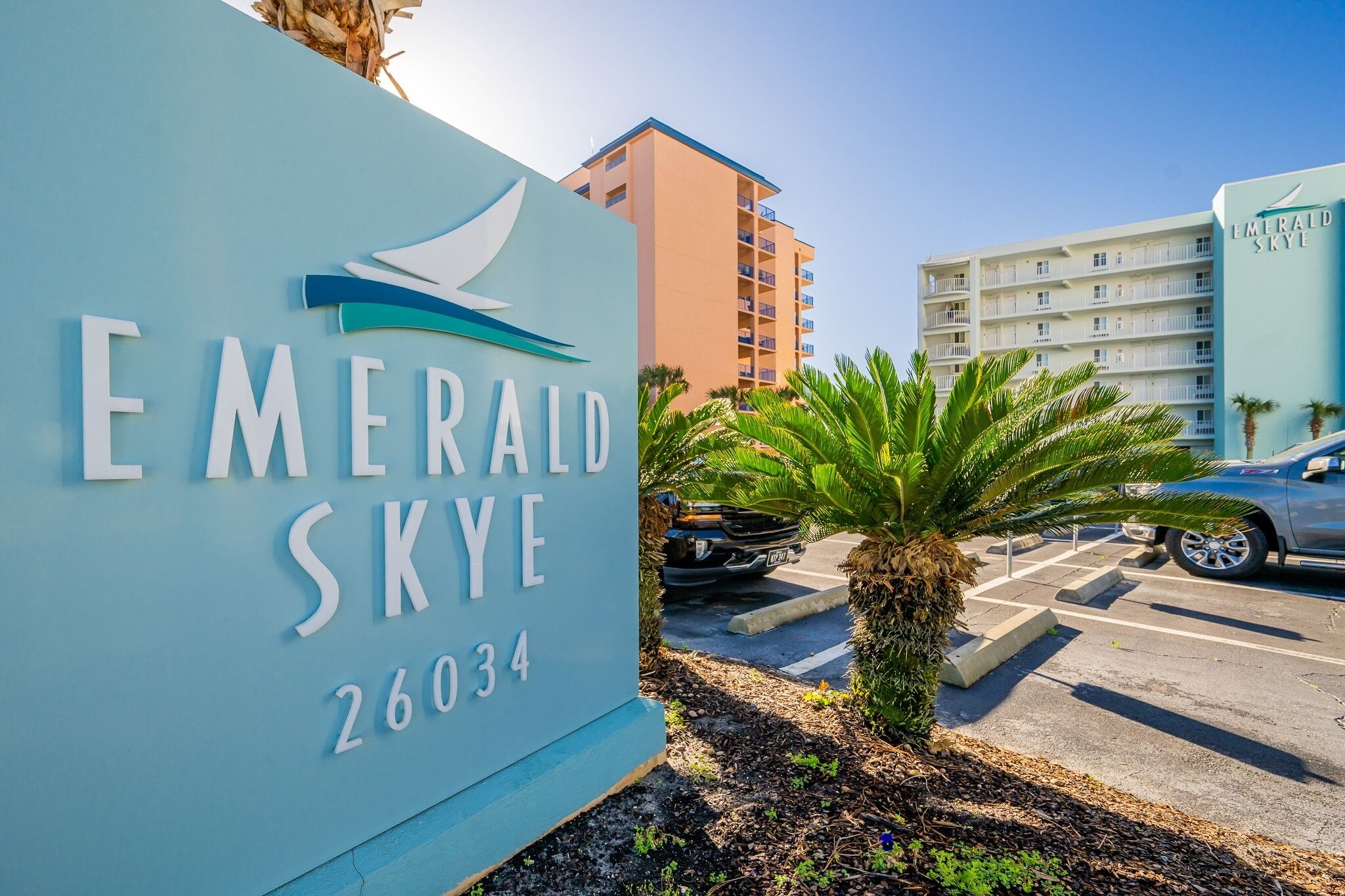 Skilt for Emerald Skye med et moderne design, der viser en palme og en parkeringsplads med biler.
