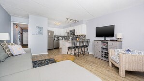 A compact living space with a kitchenette, a dining area, and a seating area with a television. - Emerald Skye 63 1 Bedroom Condo (Orange Beach)